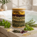Glass jar with layered dried herbs on a stone surface with fresh herbs around