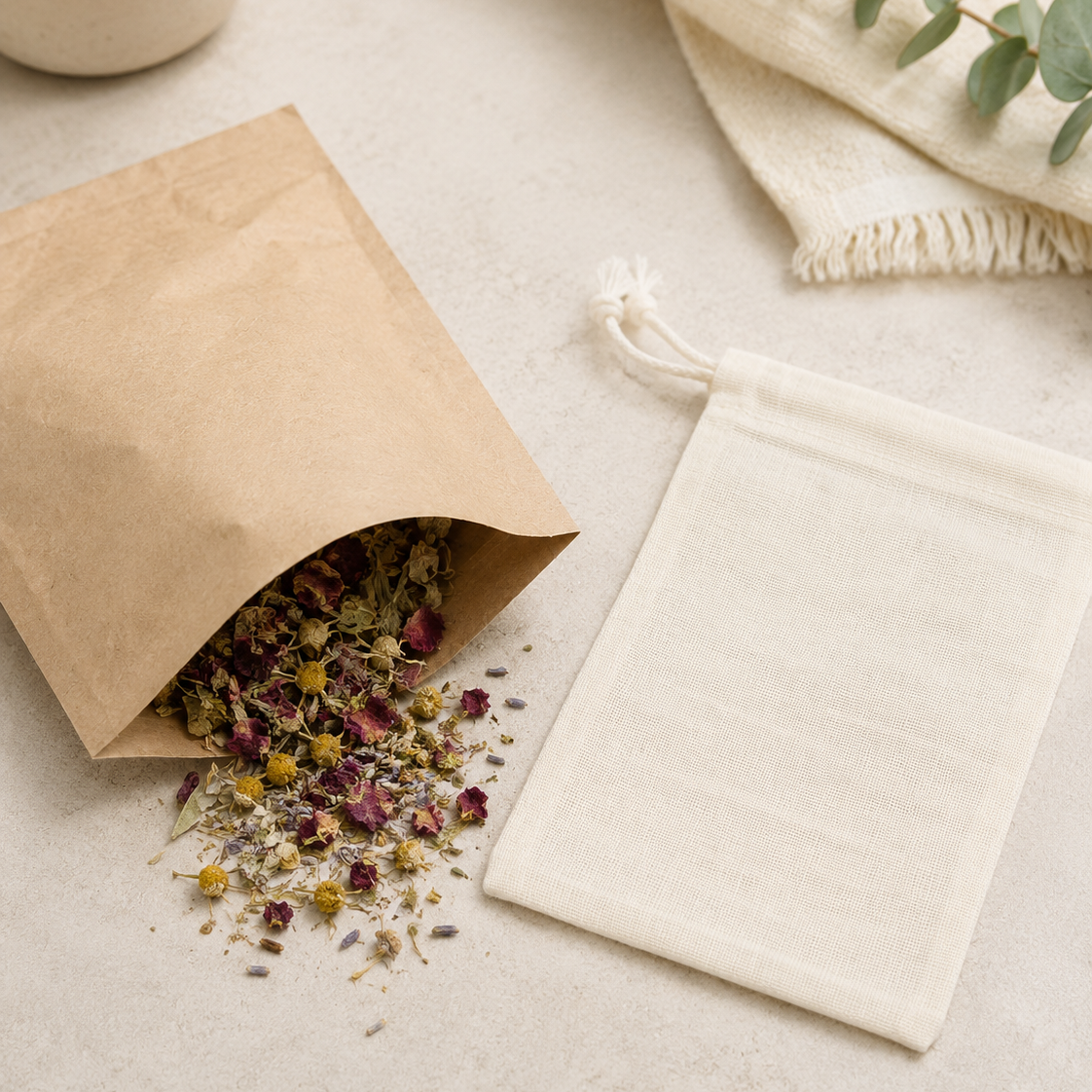 Kraft paper refill bag lying open with loose botanical bath herbs spilling onto a neutral tabletop beside a flat, empty cotton muslin steeping bag.